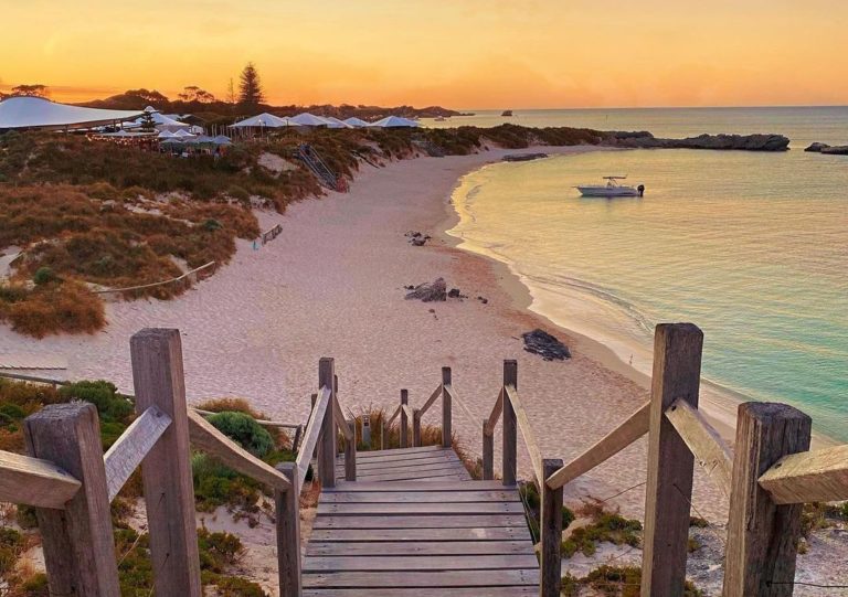 A panoramic view of a pristine beach on Rottnest Island, with turquoise waters and white sand stretching into the distance.