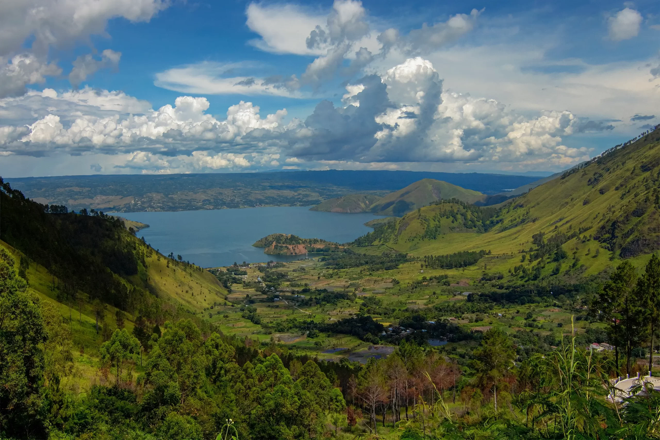 A panoramic view of Lake Toba, showcasing its turquoise waters and surrounding lush green mountains.