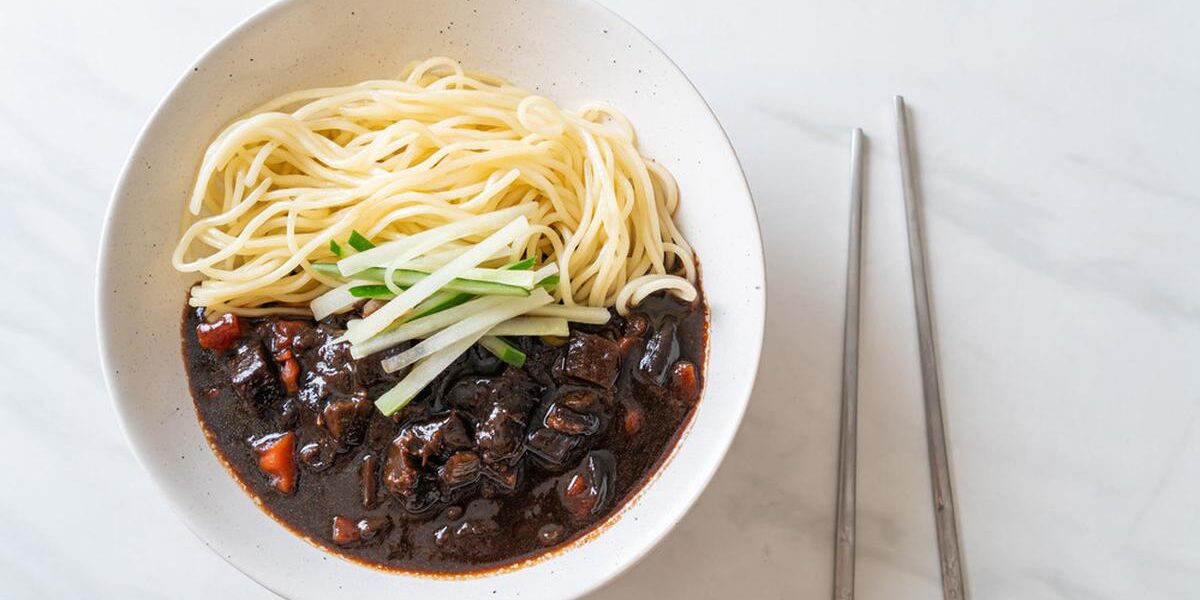 Seporsi jajangmyeon dengan saus kacang hitam yang kaya rasa, disajikan dengan acar lobak kuning dan mi gandum tebal, menciptakan hidangan khas Korea yang otentik