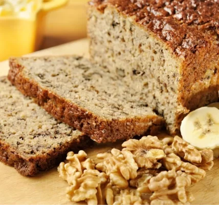 Sepotong roti pisang panggang yang lembut, disajikan dengan potongan pisang segar dan taburan kacang almond